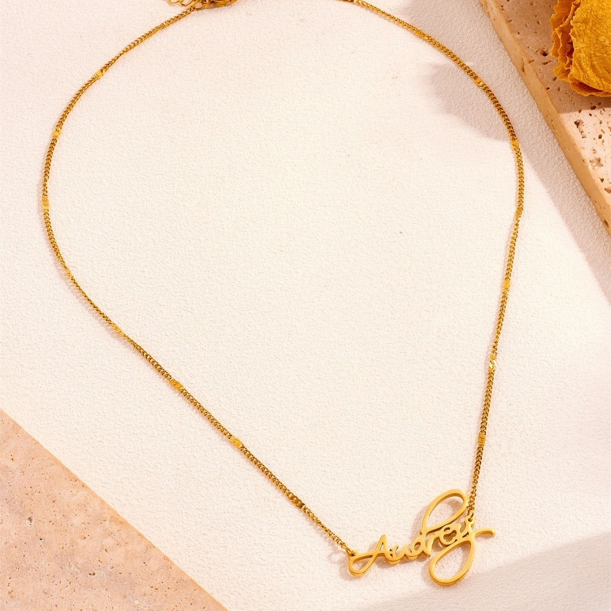 Gold script name necklace laid flat on cream background