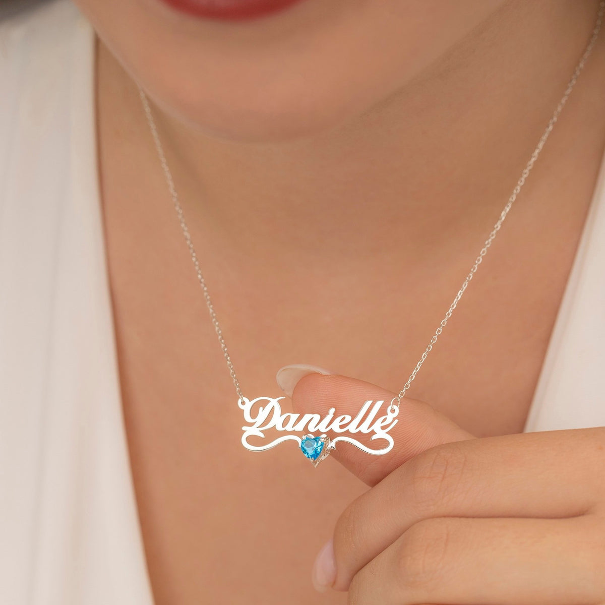 Model wearing silver name necklace with blue heart birthstone