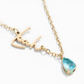 Gold name necklace with blue teardrop birthstone on white background